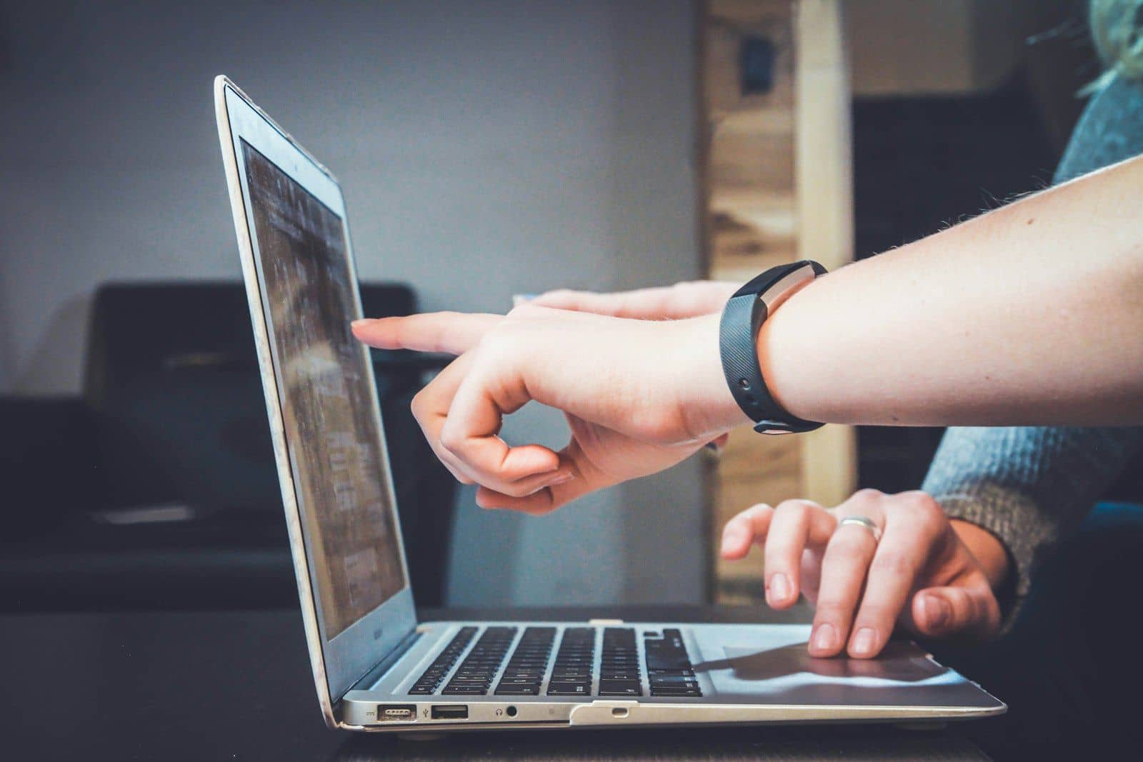 A hand pointing at a laptop screen while another hand types