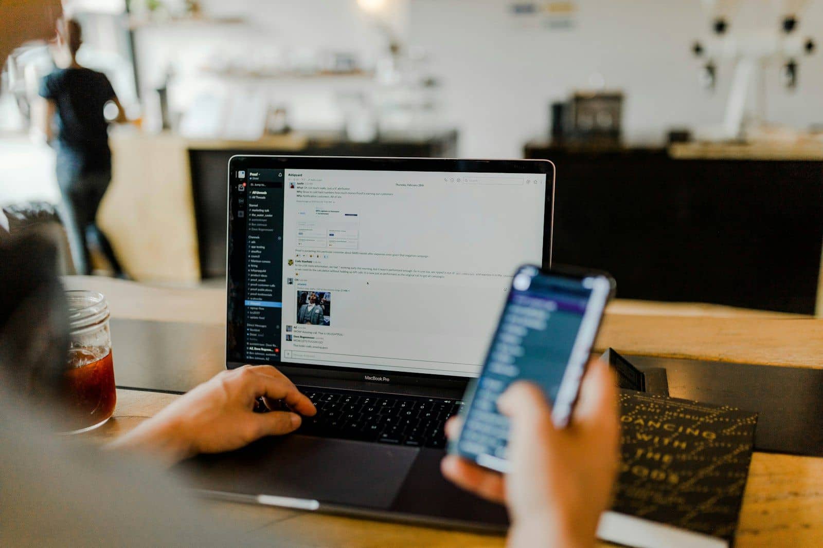 A person using a laptop and a phone together at a cafe table