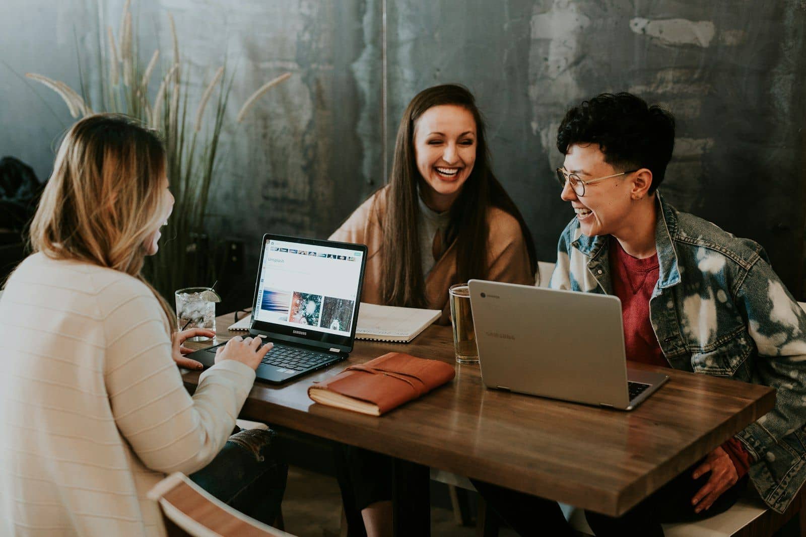 Three young people laughing together while working on laptops